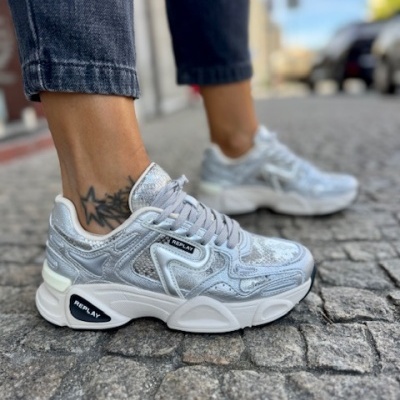 Ténis prateados e brancos REPLAY usados em rua com calçada portuguesa