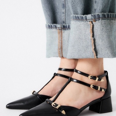 Sapatos pretos de salto médio com tiras e fivelas douradas, calças de ganga azul claro