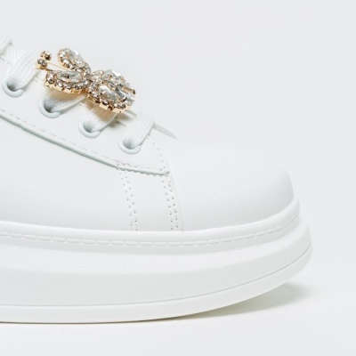 Sapatilha branca com acessório dourado e pedras sobre atacadores