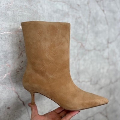 Bota camel de camurça com salto fino sendo segurada por uma mão