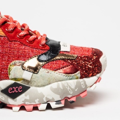 Sapatilha esportiva vermelha com detalhes metálicos e sola branca com padrões cinzentos e rosa.