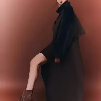 Mulher a vestir casaco longo preto com mangas de pelo azul escuro e botas castanhas