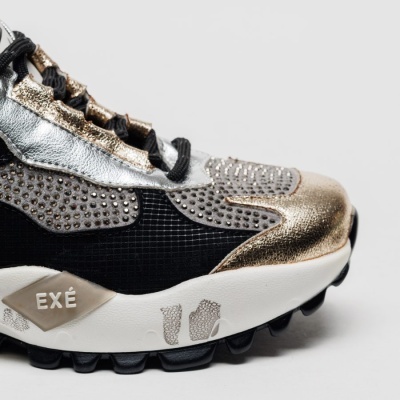 Sapatilha desportiva preta, dourada e prateada com sola branca e o texto EXÉ