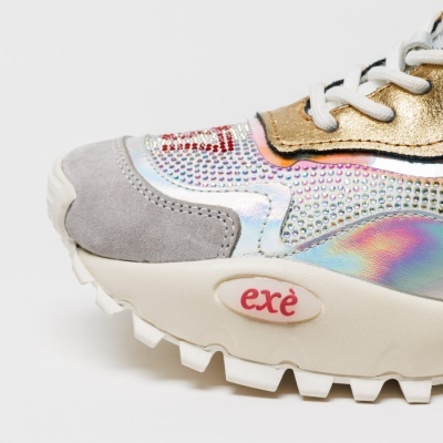 Ténis com detalhes em camurça cinza, holográfico e dourado, texto exè na sola