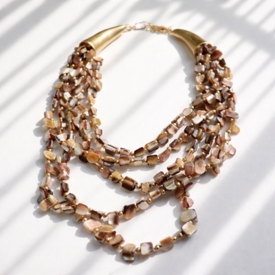 Colar de contas castanhas e douradas sobre fundo branco com sombras