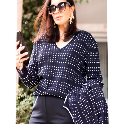 Mulher com blusa preta de malha com padrão branco e óculos de sol grandes