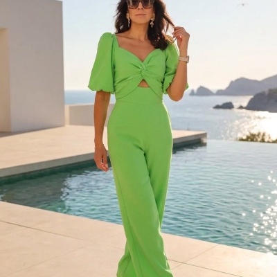 Mulher com macacão verde de mangas bufantes junto a uma piscina com vista para o mar