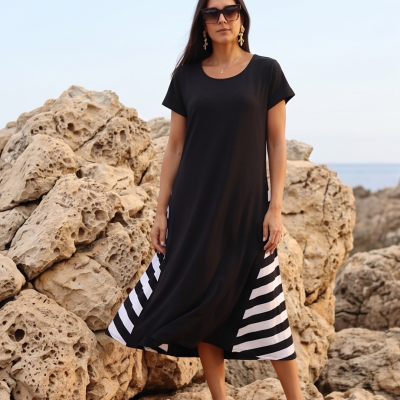Vestido midi preto com riscas brancas na parte inferior num cenário rochoso costeiro.