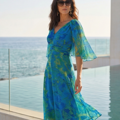 Vestido midi azul com padrão verde, mangas transparentes, decote em V, vista para o mar e piscina