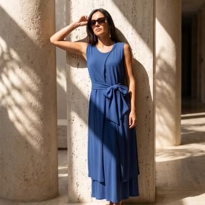 Vestido comprido azul com cinto largo e mulher com óculos escuros perto de colunas de pedra
