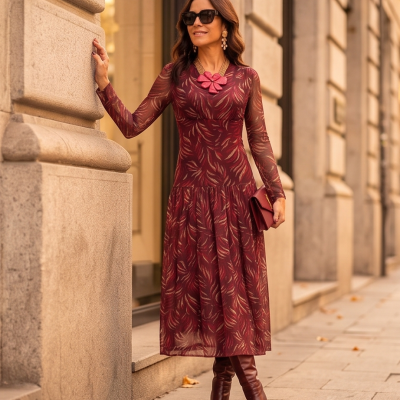 Mulher com vestido vermelho comprido de padrão de penas, botas castanhas, óculos escuros, colar rosa e mala vermelha na mão