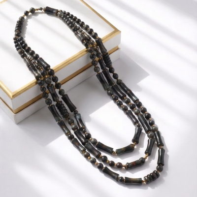 Colar com contas negras e douradas várias voltas sobre caixa branca com bordas douradas