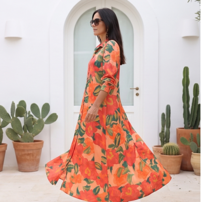 Mulher com vestido longo floral salmão e laranja, usando óculos escuros, em varanda com plantas e cactos