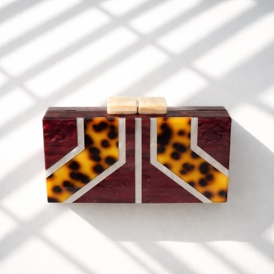 Clutch retangular rígida com padrão geométrico castanho, amarelo e branco perolado.