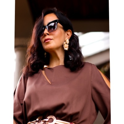 Mulher com vestido castanho e acessórios dourados e brancos