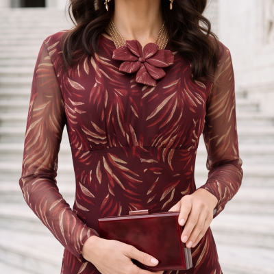 Vestido bordô com padrão de folhas douradas, colar com flor, brincos dourados e clutch bordô
