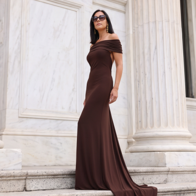 Mulher com vestido longo castanho escuro ombro a ombro em escadaria de mármore