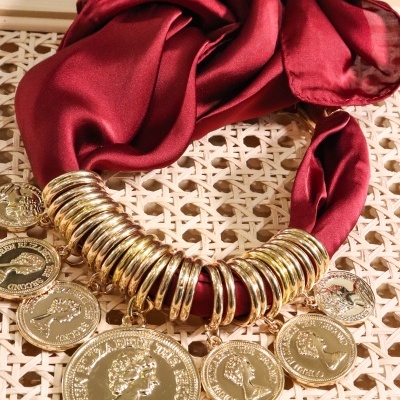 Lenço vermelho com argolas douradas e moedas decorativas sobre tecido de palha entrelaçada