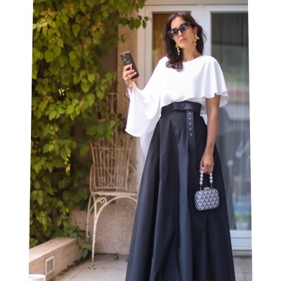 Mulher com vestido preto e branco, pequena mala cinza geográfica e óculos escuros em exterior