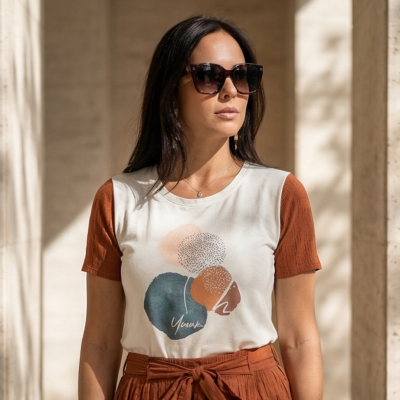 Mulher vestindo t-shirt branca com mangas terra e estampa colorida, com saia ou calça terracota de cintura alta com cinto.