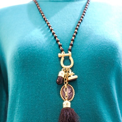 Colar dourado com pendentes e pendente de pelo castanho numa camisola verde água.