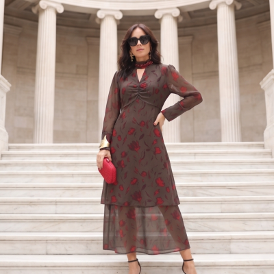 Mulher usando vestido midi transparente com flores vermelhas, clutch vermelha e óculos escuros em escadaria com colunas.