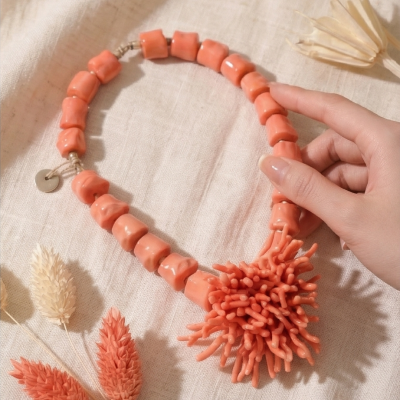 Colar de pedras de coral rosa sobre tecido bege com flores secas