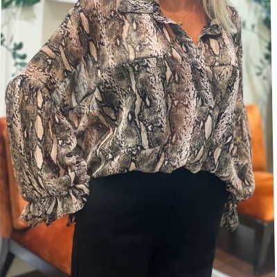 Blusa com padrão de pele de cobra e calças pretas em ambiente interior