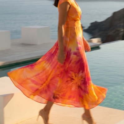 Vestido midi fluído em tons de laranja, amarelo e rosa com estampa floral e sapatos nude de salto alto