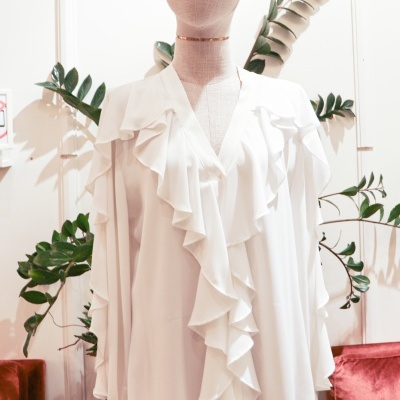 Blusa branca com folhos num manequim com plantas ao fundo