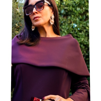 Mulher de vestido roxo escuro, brincos dourados, óculos escuros e bandeja retangular em padrão misto.