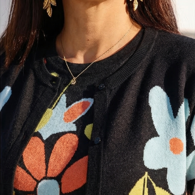 Cardigã preto com flores coloridas, brincos dourados de folhas e colar delicado