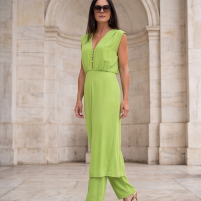 Mulher com vestido e calças verdes e sandálias douradas em ambiente de mármore