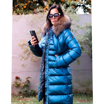 Mulher com casaco acolchoado azul com capuz de pelo castanho a segurar telemóvel