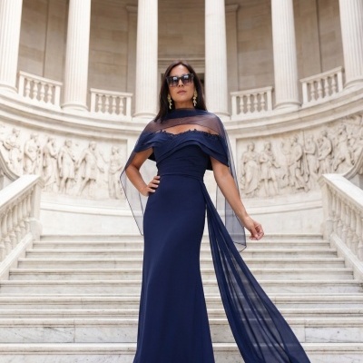 Vestido longo azul-marinho com faixa transparente e sandálias, mulher na escadaria clássica branca