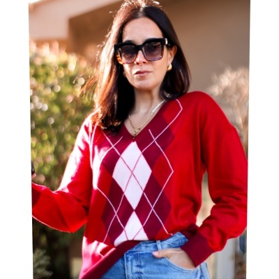 Mulher com camisola de malha vermelha com padrão de losangos, decote em V, e jeans azuis claros