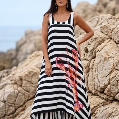 Mulher em vestido riscado preto e branco com estampa de lagosta, em ambiente rochoso à beira-mar