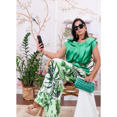 Mulher com roupa verde e branca, óculos escuros, sentada numa cadeira com planta ao fundo