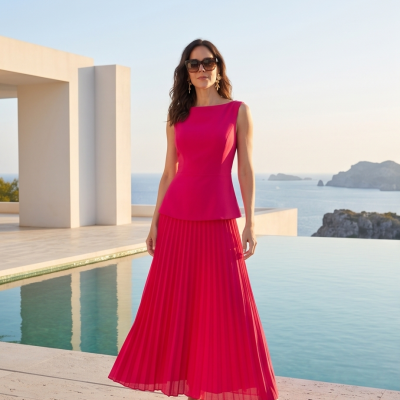 Vestido longo feminino rosa com saia plissada e parte superior lisa sem mangas, usado com sandálias de salto junto a uma piscina.