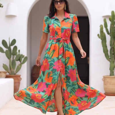 Vestido longo floral colorido com cinto e botões, usado por mulher com óculos escuros num ambiente exterior.