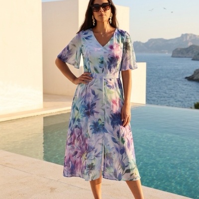 Vestido midi floral azul e roxo com cinto usado por mulher ao lado de piscina com vista para o mar