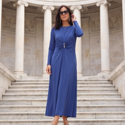 Mulher a usar vestido azul comprido com detalhe franzido e aplicação brilhante, sandálias bege, em escadaria com colunas de pedra.