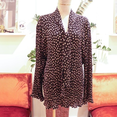 Blusa preta com bolinhas cor-de-rosa em manequim em loja com sofás laranja e plantas