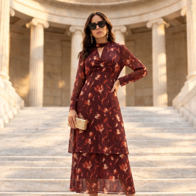 Mulher com vestido floral comprido castanho em escadas de mármore com colunas neoclássicas ao fundo