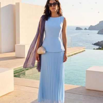 Mulher com vestido azul claro e acessórios junto a piscina num cenário exterior.