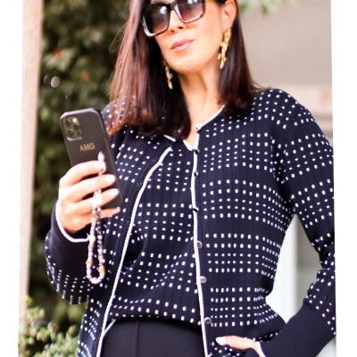 Cardigã preto com pontos brancos e botões, usado com calças pretas e acessórios dourados