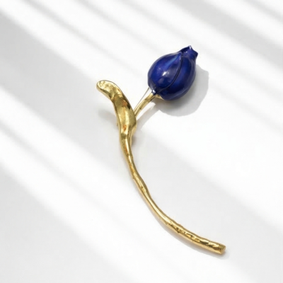 Broche em forma de flor dourada com botão azul sobre fundo branco