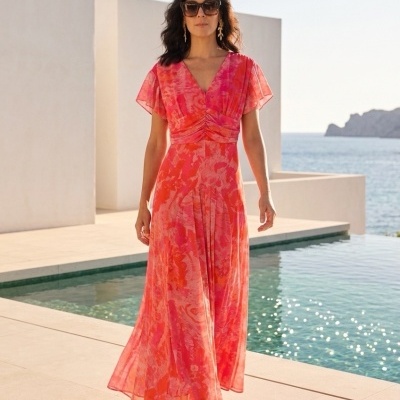 Vestido comprido com padrão vermelho e rosa em mulher junto a piscina e mar