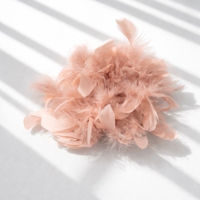 Adereço de cabelo de penas cor de rosa claras sobre superfície branca com luz natural.