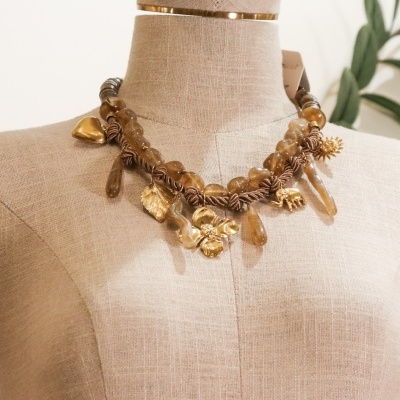 Colar com contas castanhas e pendentes dourados em manequim bege